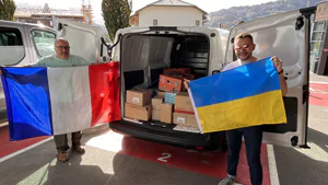 A SYVECO employee in front of a van carrying donations for Ukraine. He is holding a Ukrainian flag.