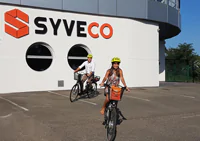 two SYVECO employees riding electric bikes in front of the building